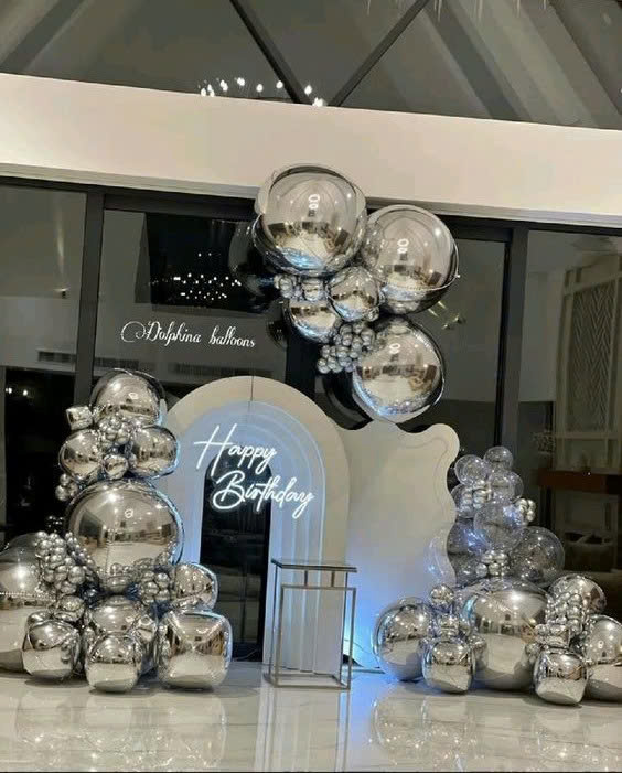 Mẫu **backdrop sinh nhật sang trọng** tone bạc ánh kim, kết hợp bóng bay metallic và đèn LED tạo không gian hiện đại, nổi bật.